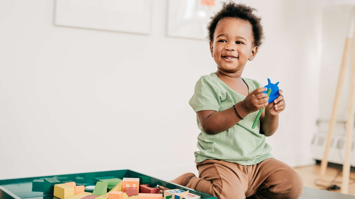 Smiling toddler playing with colorful wooden blocks, engaging in sensorimotor play for early development