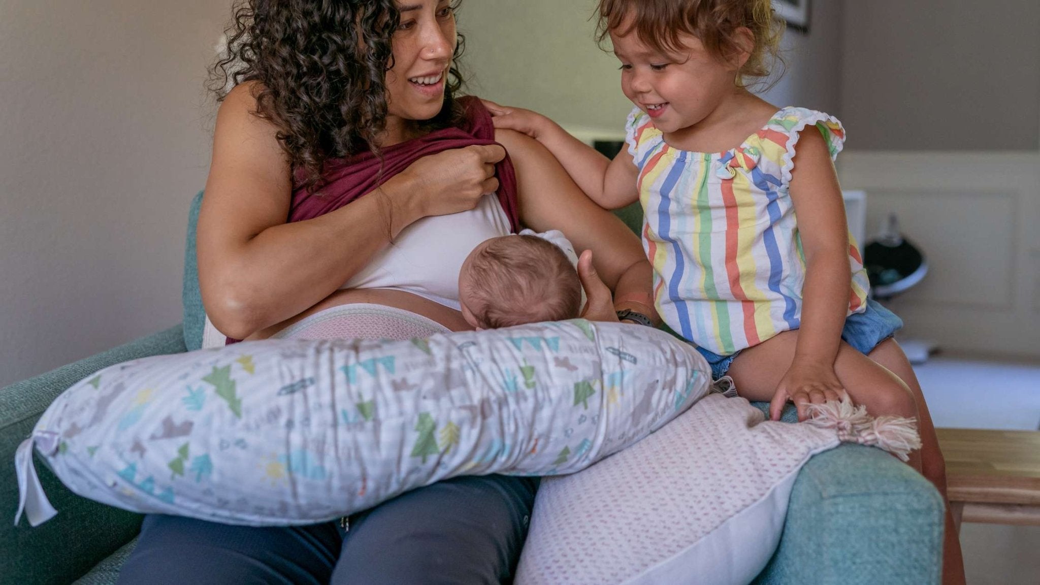 Mother breastfeeding newborn while older sibling watches, showing the connection and complexity of feeding in early parenthood