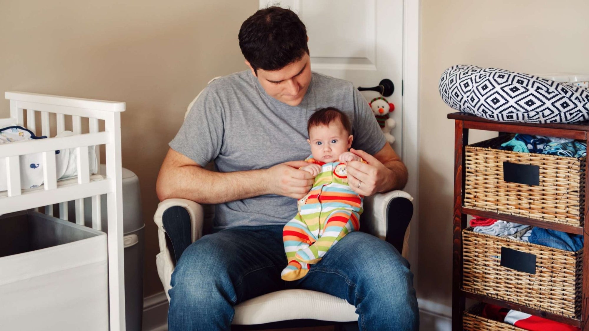 A father holding his alert, wide-eyed baby in a nursery chair, representing early infant sleep challenges during the 4-month sleep progression.
