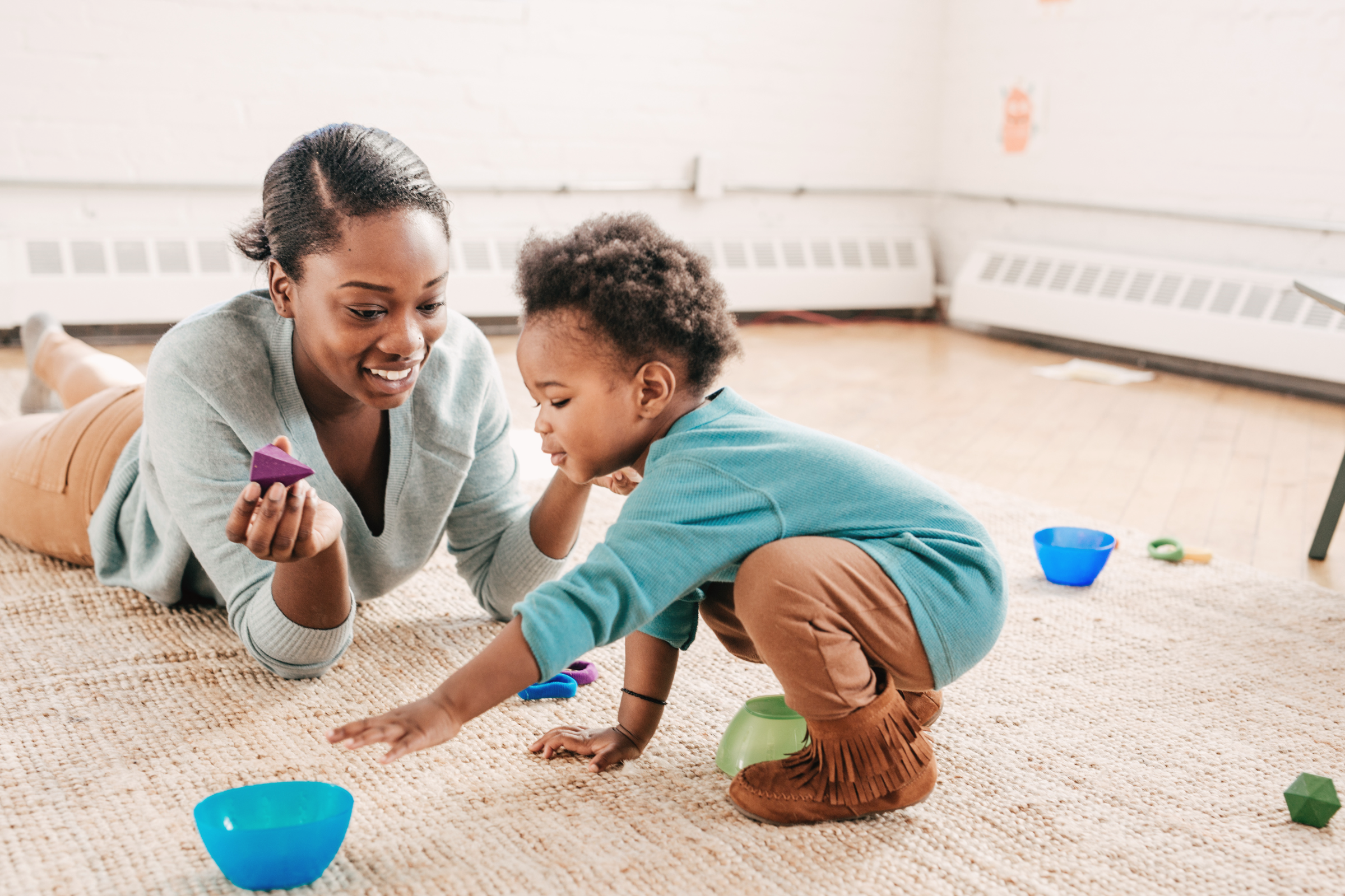 Mother playing on the floor with her child using simple developmental toys, illustrating the best toys for child development based on Piaget’s stages of play