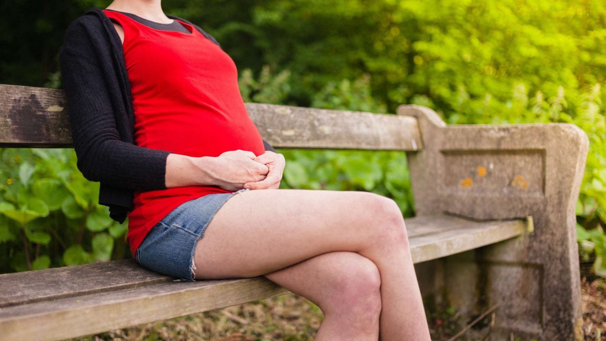 Pregnant person sitting on a park bench with hands on their belly, reflecting on body changes during pregnancy