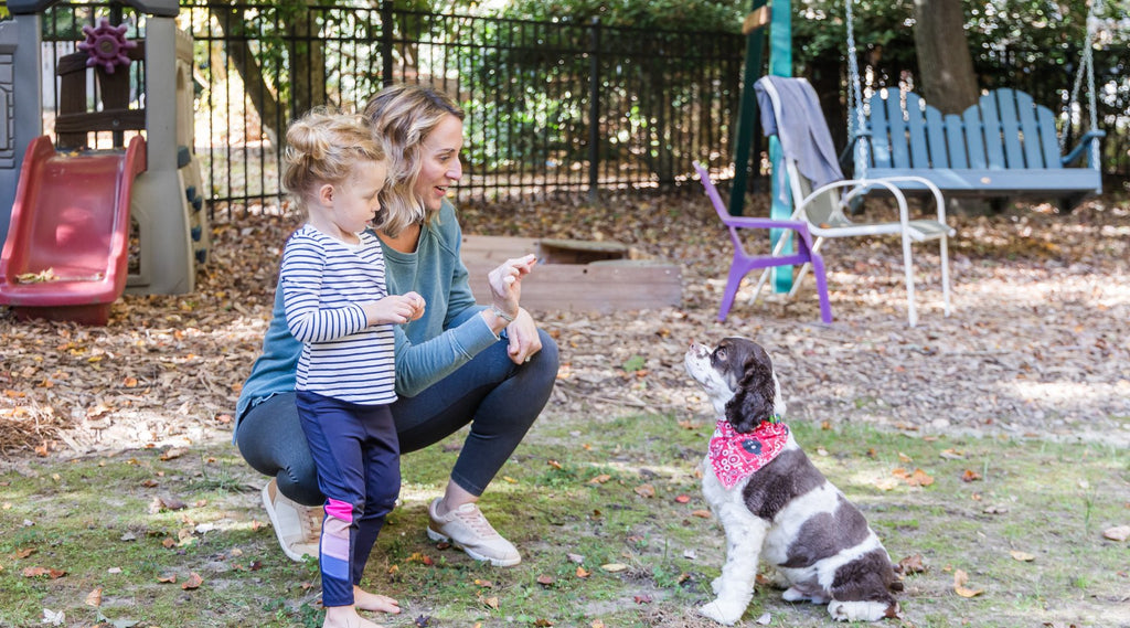 Mom and toddler teaching dog to sit in backyard