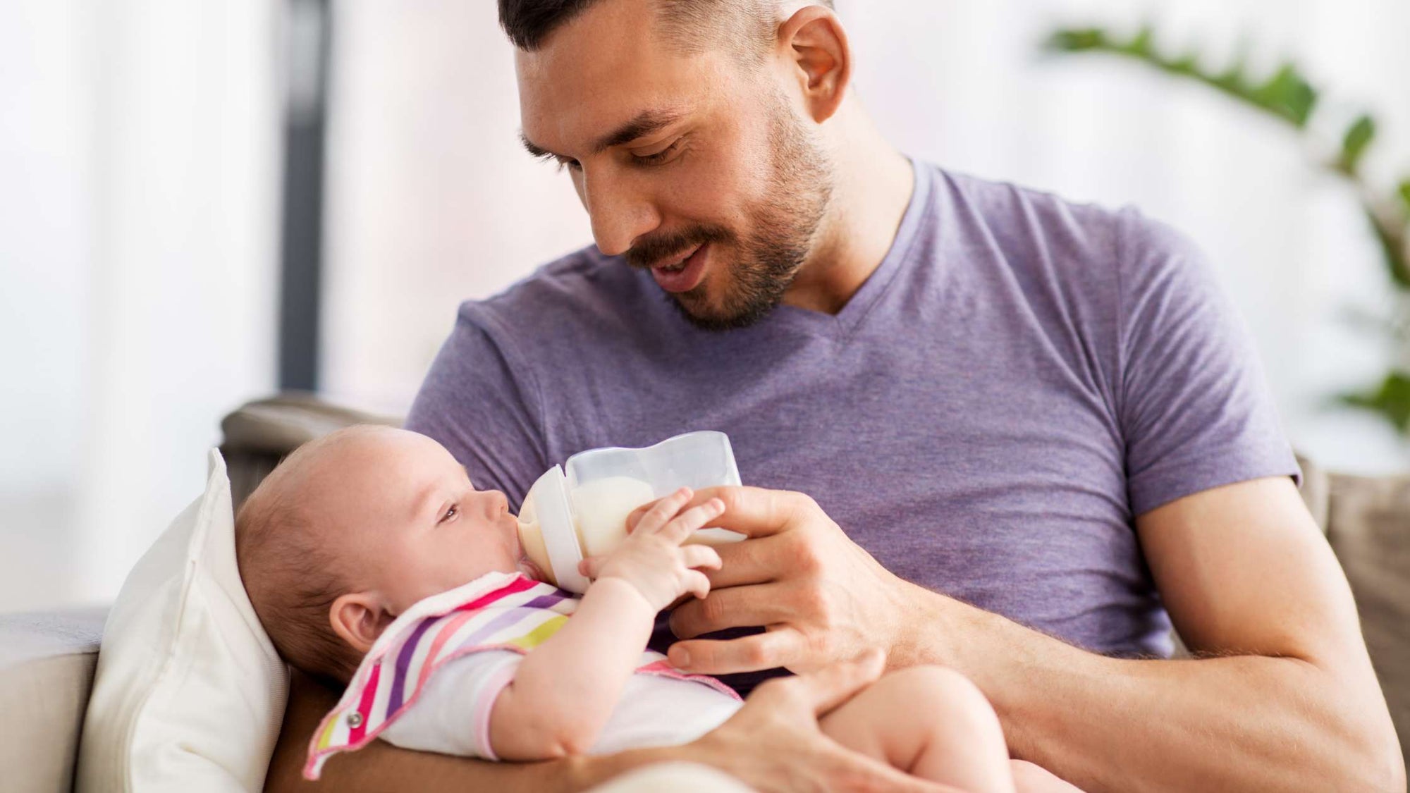 Father bottle-feeding infant at home, showing bonding and shared infant care through combination feeding